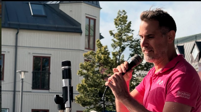 Andreas Barås leder allsång med mikrofon utomhus på ett torg.