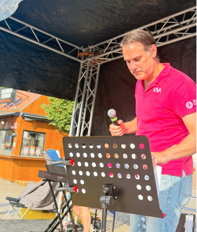 Andreas Barås vid ett notställ med mikrofon under allsången.
