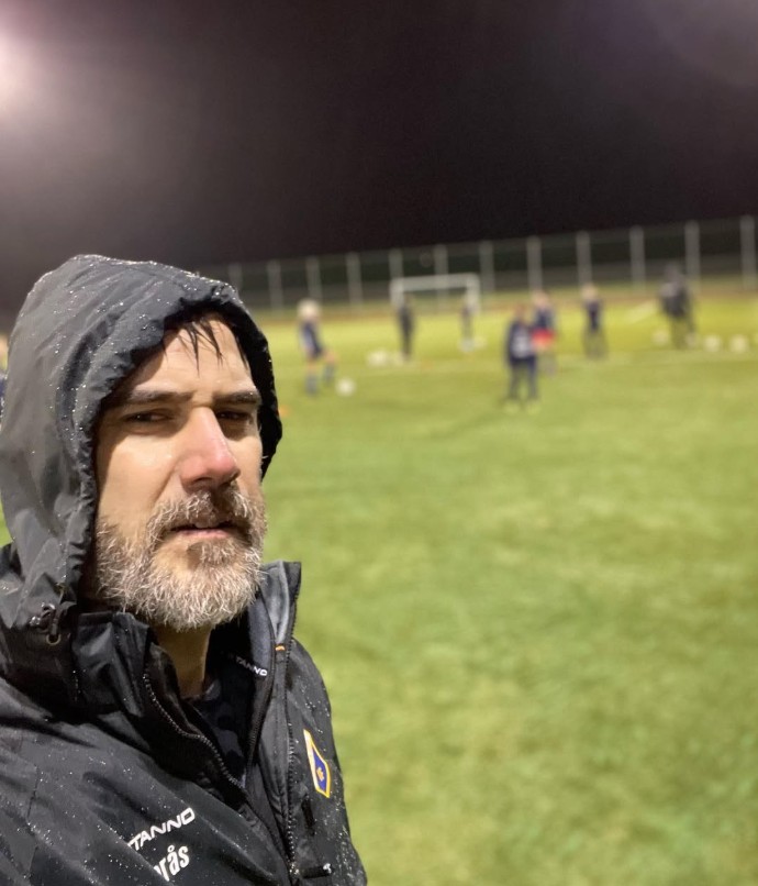 Andreas Barås i huvtröja på en fotbollsplan i kvällsljus.