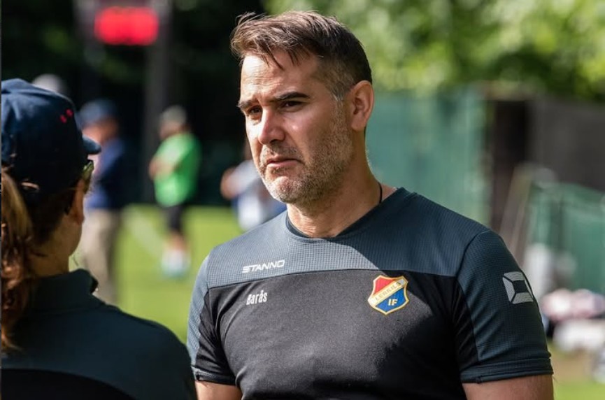 Andreas Barås i klubbtröja i samtal med andra på en fotbollsplan.