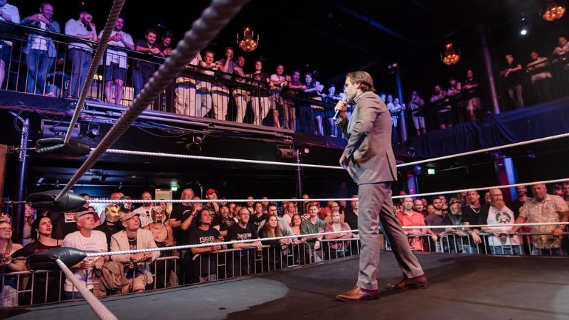 Andreas Barås med mikrofon i en wrestlingring inför publik.