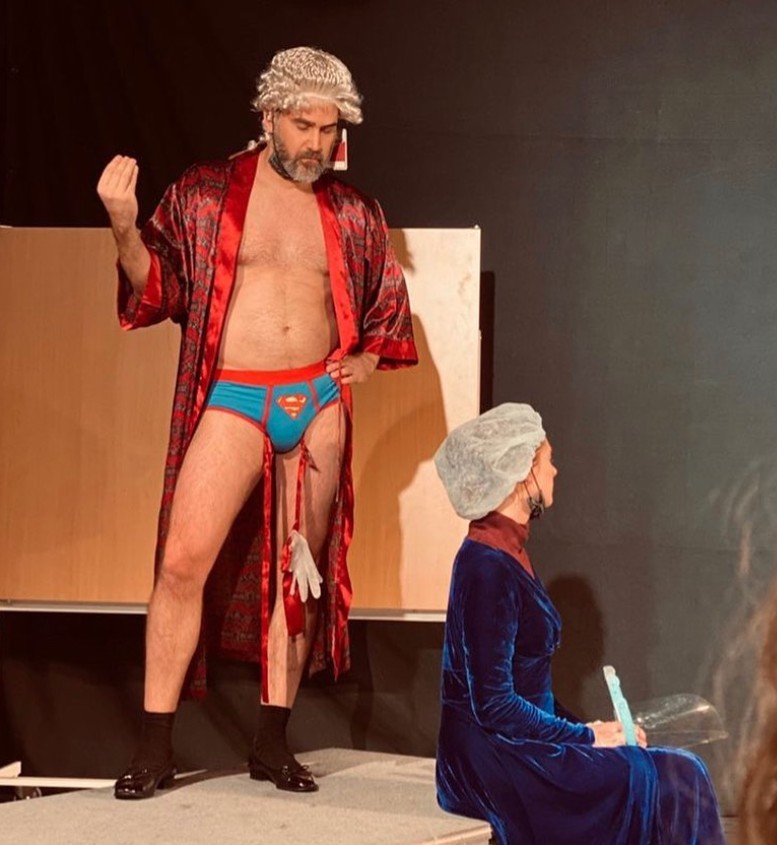 Andreas Barås i peruk och röd morgonrock i en komediscen.